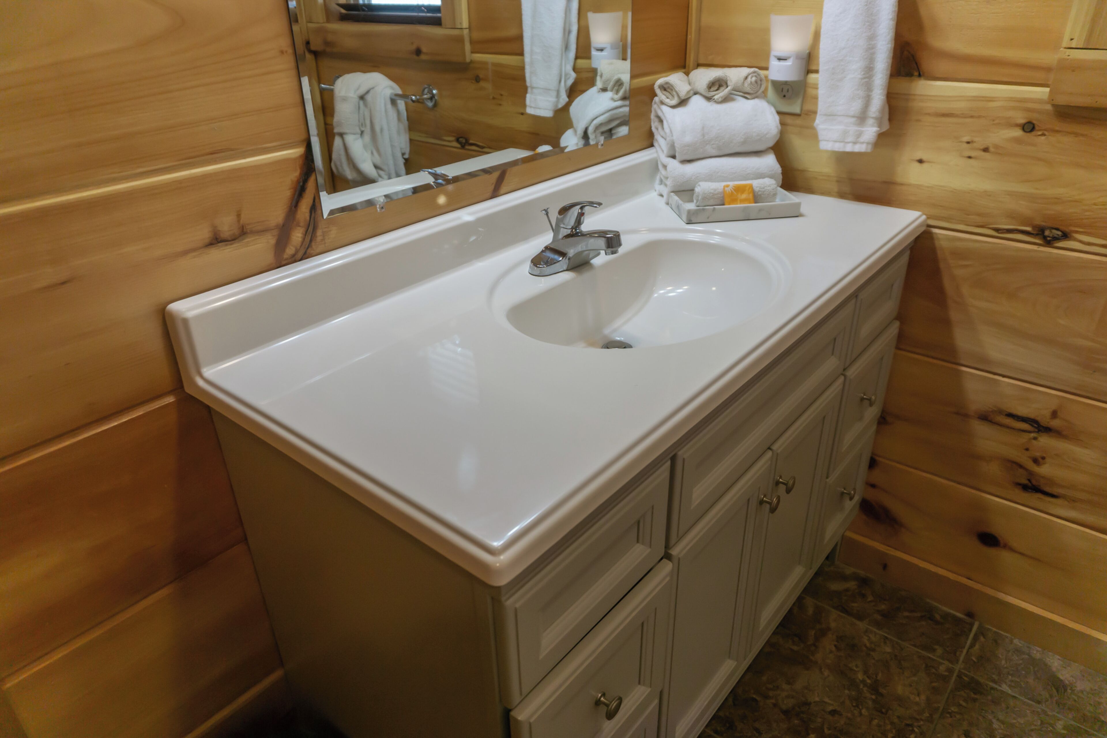 A wooden cabin-style bathroom with a white sink, wooden cabinets, and a mirror reflecting towels.