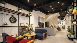 A modern lounge area with a dartboard, seating, a kitchen area, and potted plants. - Laverne Boutique - D1 City Center (Ho Chi Minh City)