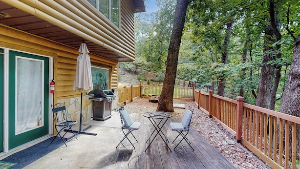 A wooden deck with two chairs and a table, surrounded by a wooden fence and trees. - Lake of the Ozarks Apt 3 Mi to Dtwn Shops & Dining (Lake Ozark)