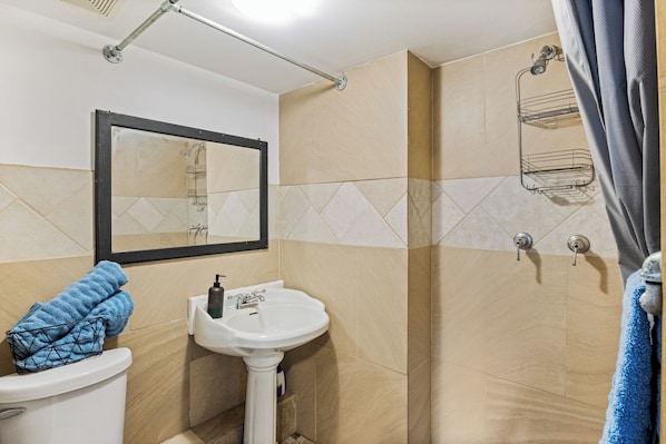 A bathroom with a toilet, sink, mirror, shower, and towel rack. - Lake of the Ozarks Apt 3 Mi to Dtwn Shops & Dining (Lake Ozark)