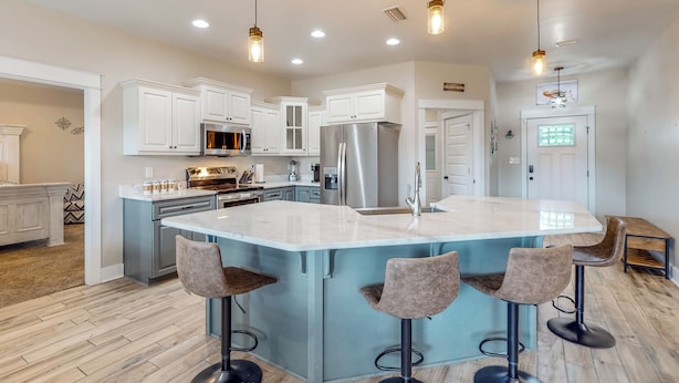 Una cocina moderna con armarios blancos, electrodomésticos de acero inoxidable y una isla central con taburetes de bar.
