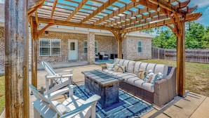 Un patio cubierto con una pérgola de madera, mobiliario exterior y una mesa de piedra.