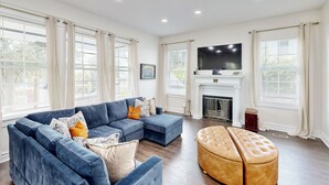A living room with a sectional sofa, ottoman, fireplace, and large windows. - < 2 Mi Dtwn Augusta: Charming Historic Home (Augusta)