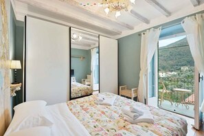 Un dormitorio con cama, espejo, balcón con mesa y sillas, y vistas a una ladera.