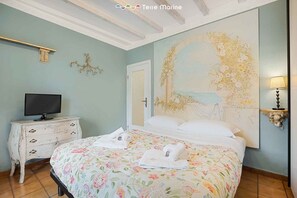 A bedroom with a floral bedspread, a television on a dresser, and a large floral painting on the wall. - Welcome to La Petite - a delightful holiday home offering you a welcoming and intimate experience. Located in a quiet area, La Petite is the perfect refuge for those seeking a moment of relaxation and serenity.The property is equipped with all the esse (La Spezia)