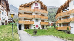En bygning med flere etager, træbalkoner, et skilt med teksten "Lehnstrasse" og et bjergrigt landskab i baggrunden.