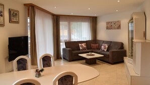 En moderne stue med sofa, sofabord, spisebord, stole og et fjernsyn.