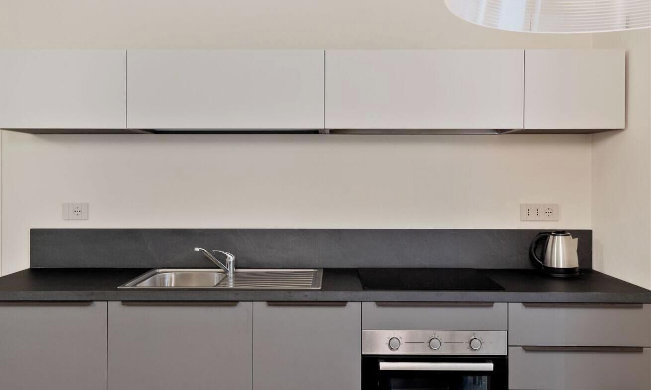 Una cuina moderna amb taulell negre, vàter d'acer inoxidable i forn integrat.