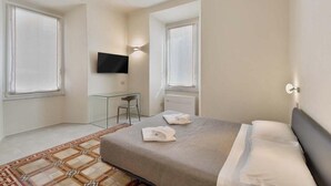 Une chambre d’hôtel moderne dotée d’un grand lit, d’un téléviseur à écran plat fixé au mur, d’un petit bureau et d’une fenêtre laissant entrer la lumière naturelle.