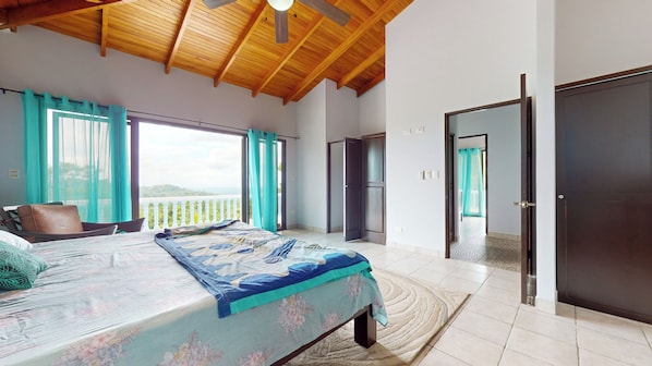 A bedroom with a bed, a view of the outdoors, a ceiling fan, and a door.