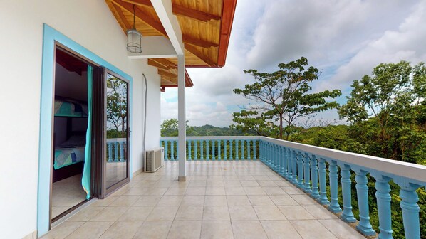 Un balcón con vistas a un paisaje exuberante, suelo de baldosas y baranda azul.