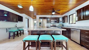 Una cocina moderna con armarios de madera oscura, una isla central con taburetes de bar, electrodomésticos de acero inoxidable y un ventilador de techo.