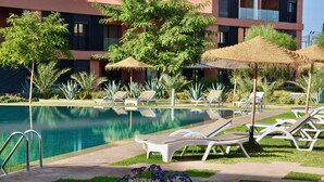 A pool area with lounge chairs, a swimming pool, and a building with balconies. - Modern 2BR/2BA Apt • Pool View Terrace • Fast Fiber WiFi • Noria Resort (Marrakech)