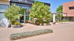 An outdoor seating area with tables and chairs in front of a building with a sign reading "Aglio e olio". - Modern 2BR/2BA Apt • Pool View Terrace • Fast Fiber WiFi • Noria Resort (Marrakech)