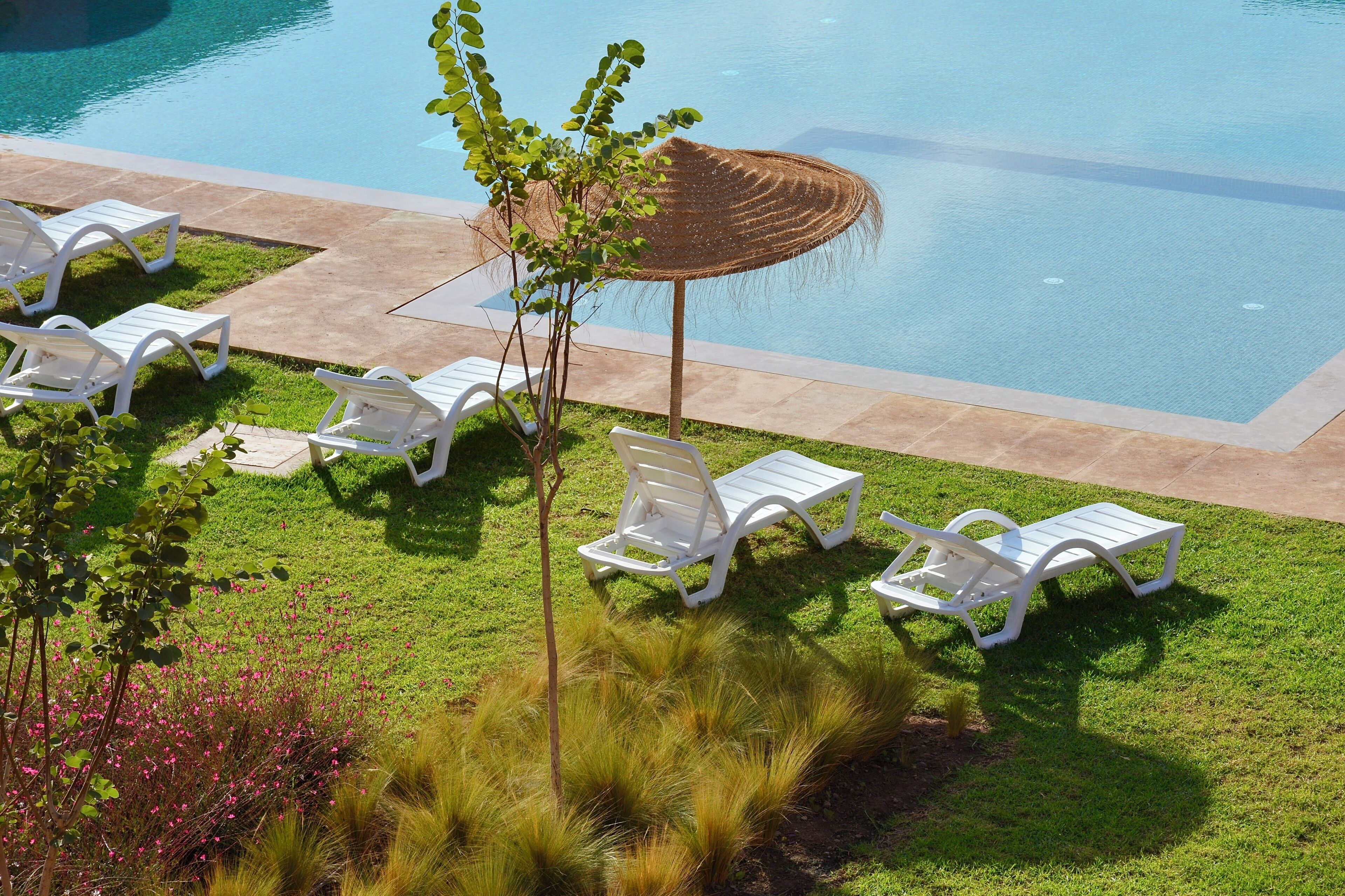 A poolside area with white lounge chairs and a large umbrella.