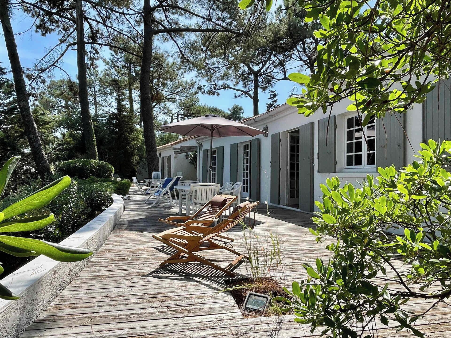 A wooden deck with lounge chairs, a covered seating area, and a building with shutters.