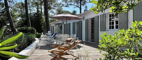 A wooden deck with lounge chairs, a covered seating area, and a building with shutters.