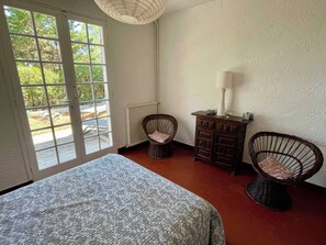 Une pièce comprenant un lit, deux fauteuils en osier, une commode et une lampe.