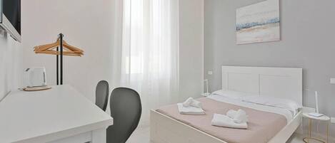 Moderni hotellihuone, jossa on sänky, yöpöytä, tuoli ja työpöytä, jossa on lamppu.