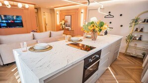 A modern kitchen with a marble countertop, built-in oven, and a central island with a sink. - Pink Perfection -  1 Bedroom Designer Apartment in Bucharest (București)