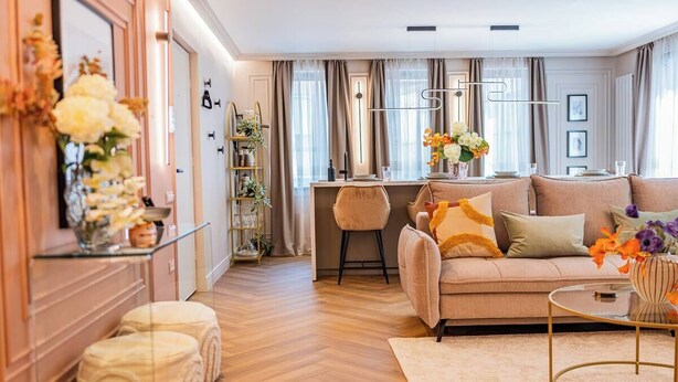 A modern living room with a sofa, ottomans, a coffee table, and a dining area with a bar. - Pink Perfection -  1 Bedroom Designer Apartment in Bucharest (București)