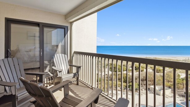 A balcony with Adirondack chairs and a table, overlooking a beach and ocean. - Surf & Racquet B170 - Hosted by Moore AI Rentals (Fernandina Beach)