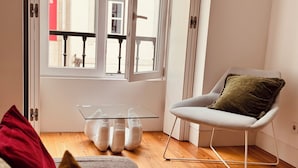 Een moderne woonkamer met een glazen salontafel, een witte fauteuil met kussen, en een houten vloer.