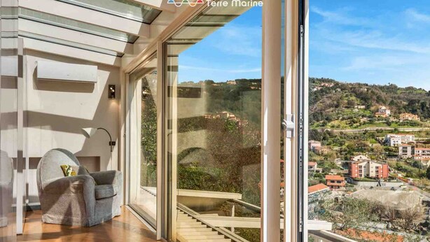 A modern interior with a glass door leading to a balcony with a view of a hillside town.