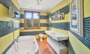 Casa de banho com paredes revestidas de azulejos amarelos e pretos, uma janela, uma banheira, sanita e lavatório.