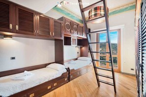 Quarto com beliches, escada de madeira e uma janela grande com vista.
