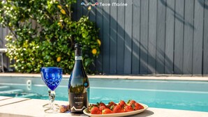 A poolside setting with a bottle of wine, a glass, and a plate of strawberries.