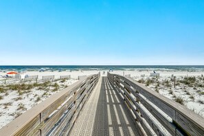 Ein Strand mit einem hölzernen Steg, der zum Wasser führt, umgeben von Sand und spärlicher Vegetation.