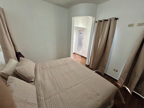 A bedroom with a bed, curtains, and a door leading to another room.