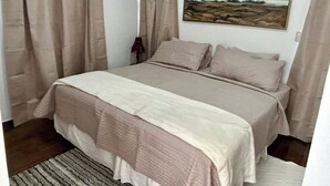 Ein Schlafzimmer mit einem Bett, beigefarbenen Vorhängen, einem Landschaftsbild und einer Lampe.