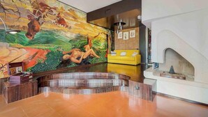 A lobby with a mural, a yellow sofa, a fireplace, and a reception desk. - Ai Colli 136, located in the renowned Zona Colli, is the perfect choice for you!This splendid property offers a large garden, ideal for relaxing in the sun, organizing outdoor dinners or simply enjoying the tranquility of the surrounding landscape.The ho (La Spezia)