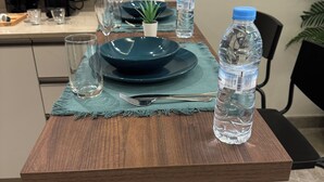 Een houten tafel met een placemat, een donkerblauw bord, een kleine plant in een pot, een waterfles en een glas.