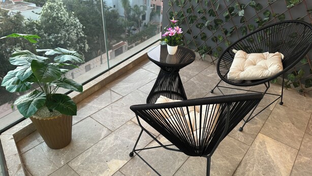 Een balkon met twee zwarte stoelen, een klein tafeltje en een bloempot.