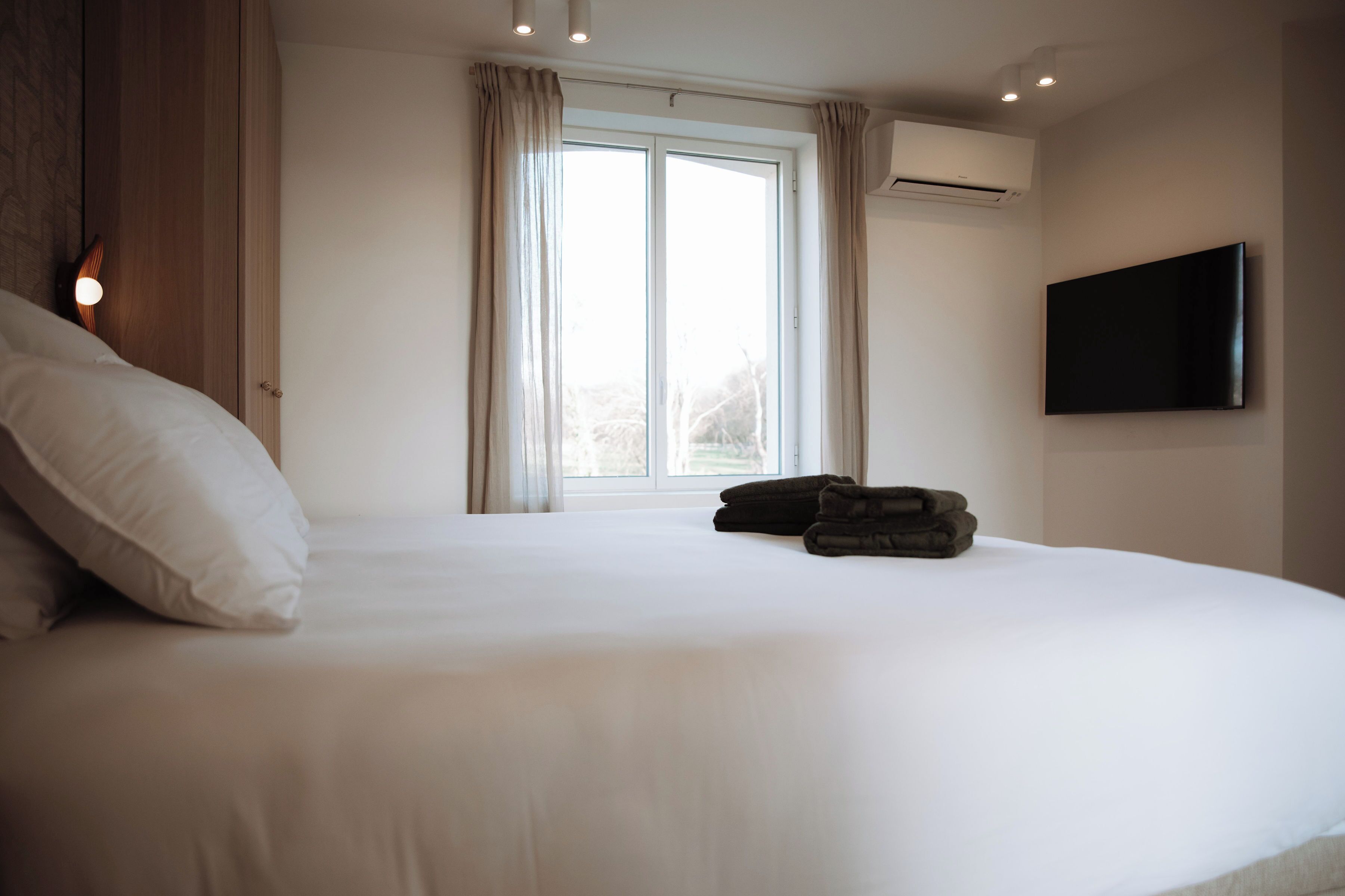 Une chambre d’hôtel avec un grand lit, un téléviseur à écran plat fixé au mur et une fenêtre avec des rideaux.