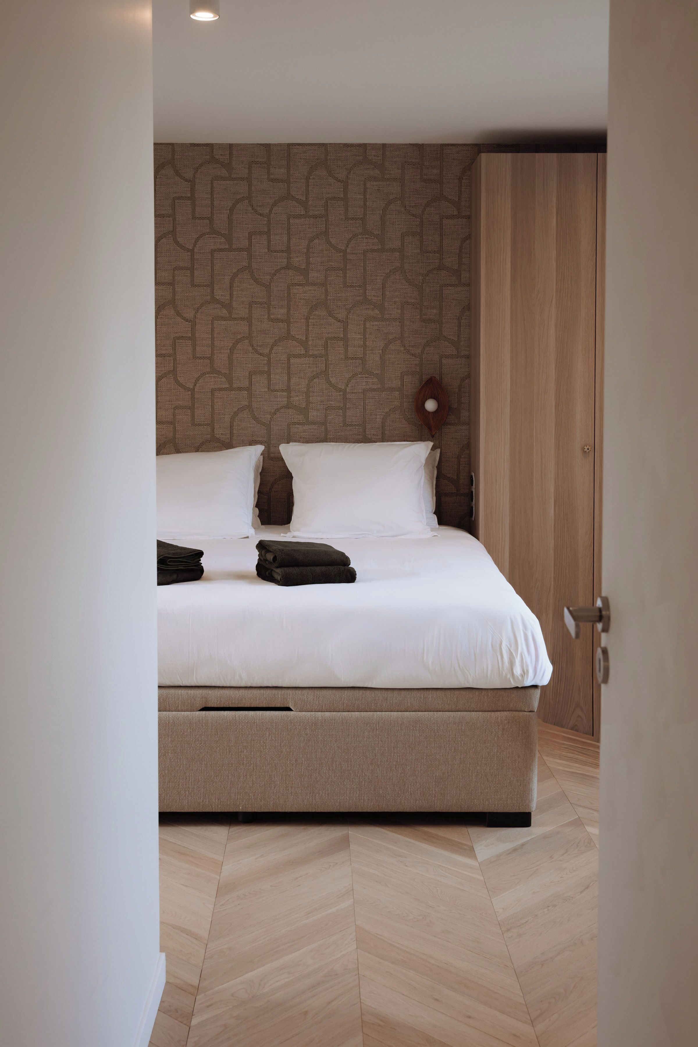 Une chambre d’hôtel moderne avec un grand lit, une armoire en bois et un mur décoré de motifs.