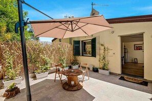 Une terrasse extérieure avec une table ronde en bois et des chaises, un parasol beige et des plantes en pot.