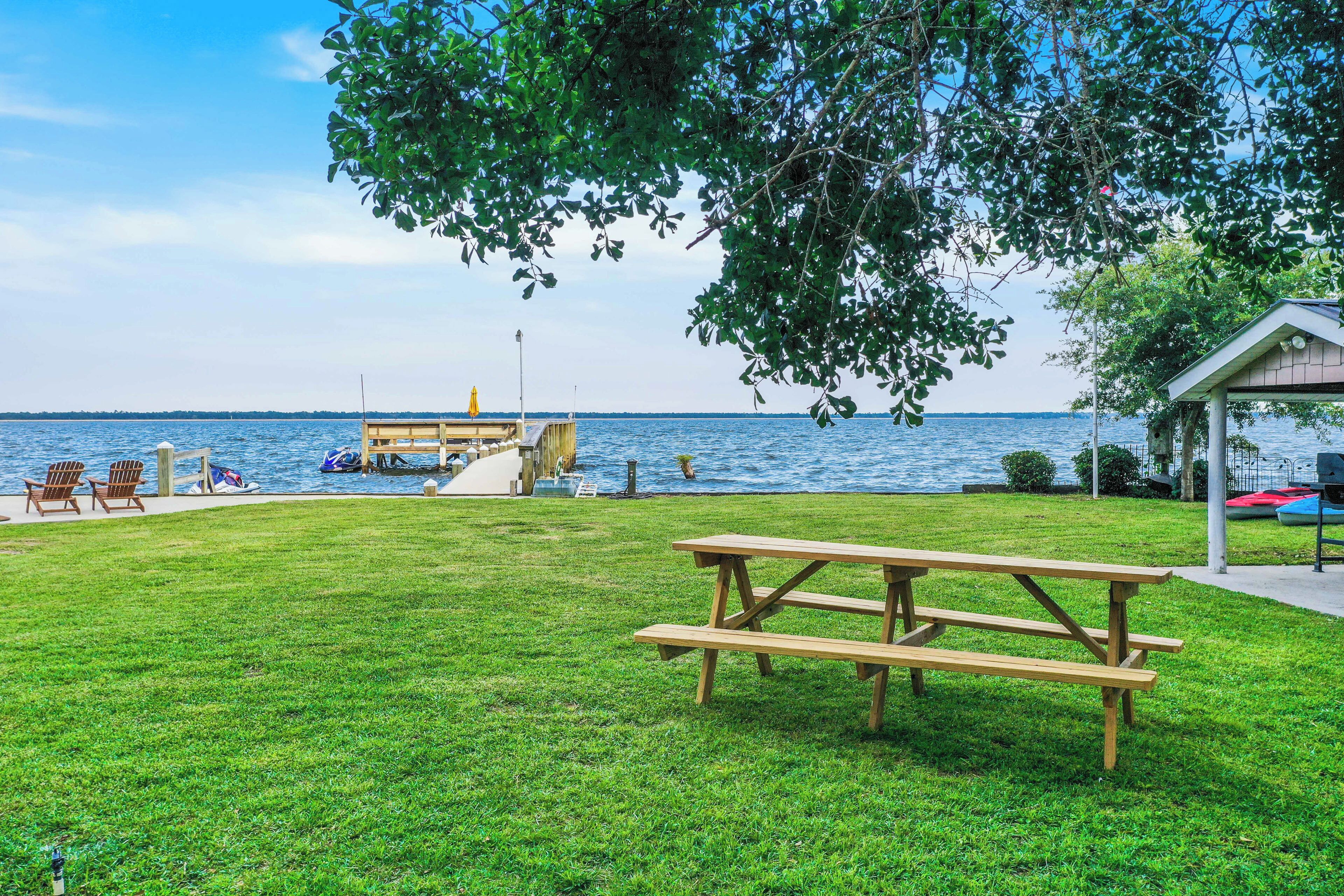 A grassy area with a picnic table, chairs, and a dock extending into the water.