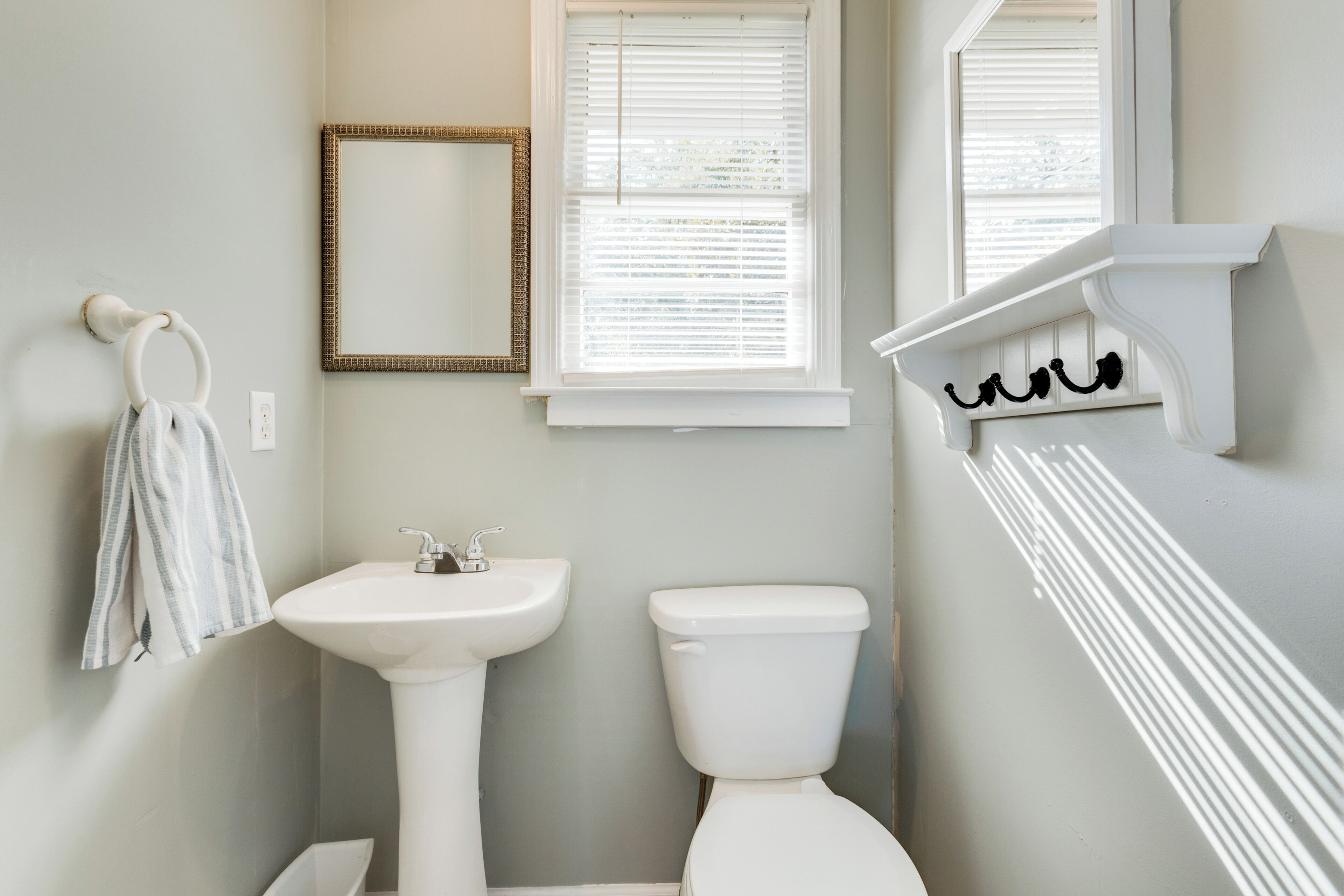 Ein Badezimmer mit einem Standwaschbecken, Toilette und einem Fenster mit Jalousien.