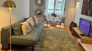 A modern living room with a green sofa, two armchairs, a coffee table, a TV, and decorative wall art. - The Crucifixo Collection - Serene (Lisboa)