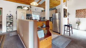A kitchen with wooden cabinets, a central island, a refrigerator, and a hanging light fixture. - Yard & Patio: Quiet & Well-Stocked Riverside Home (Three Rivers)
