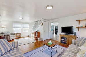 A living room with striped sofas, a television, a wooden cabinet, and a staircase. - Charming 3BR Cottage Near the Beach w/ Deck (Oak Bluffs)