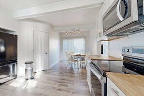 A modern kitchen with stainless steel appliances, a wooden countertop, and a dining area with a table and chairs. - Charming 3BR Cottage Near the Beach w/ Deck (Oak Bluffs)