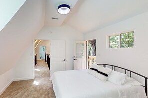Ein Schlafzimmer mit einem großen Bett, einem Fenster mit Blick auf Bäume, einer Tür zu einem anderen Raum und einer Deckenleuchte.