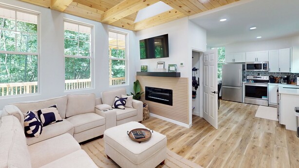 A spacious living room with a wooden ceiling, a beige sofa, and a flat-screen TV mounted above a fireplace. - Forest Views & Grill! Lynchburg Treehouse Retreat (Lynchburg)