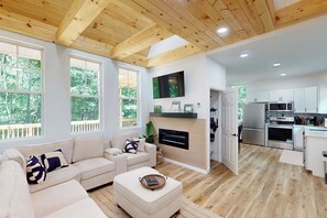 A spacious living room with a wooden ceiling, a beige sofa, and a flat-screen TV mounted above a fireplace. - Forest Views & Grill! Lynchburg Treehouse Retreat (Lynchburg)