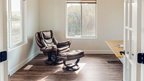 Quarto com poltrona de massagem, janela com vista para árvores e mesa de madeira.
